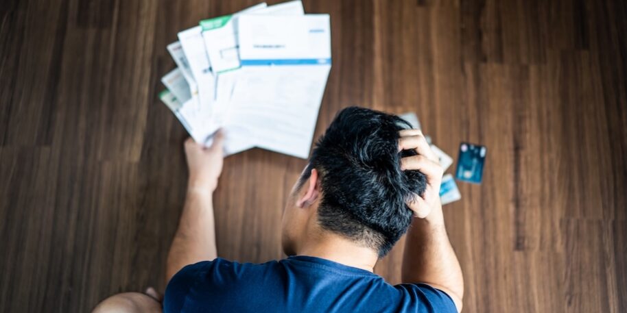 Top view of stressed young man hands holding the head trying to find money to pay credit card debt and all loan bills