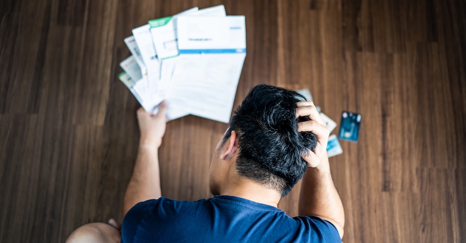 Top view of stressed young man hands holding the head trying to find money to pay credit card debt and all loan bills