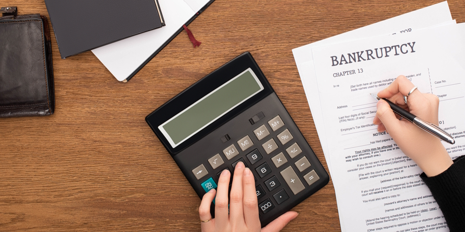 partial view of woman filling in bankruptcy form and using calcu partial view of woman filling in bankruptcy form and using calculator on wooden background
