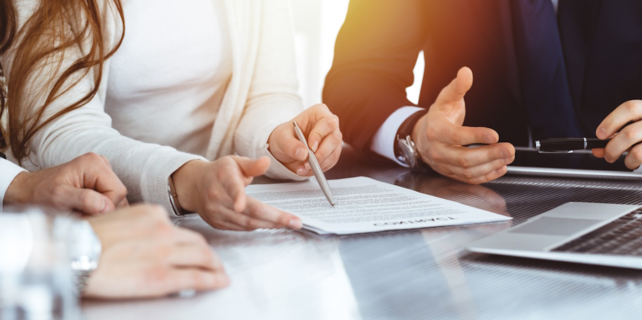 people meeting at a table with a computer and reviewing a paper document people meeting at a table with a computer and reviewing a paper document