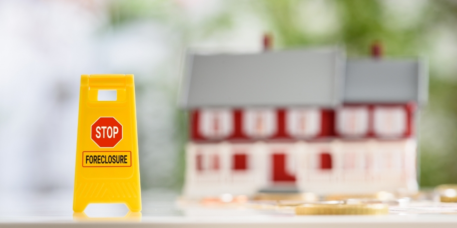 stop foreclosure a tiny model home sits in the background, with coins and a 'stop foreclosure' sign in the foreground